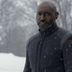 Adrian Holmes as Admiral Robert April in Star Trek: Strange New Worlds. He's wearing a black overcoat with the Starfleet Delta insignia worn as a patch on its left arm, as he stands in snowfall against the backdrop of a snow-covered forest.